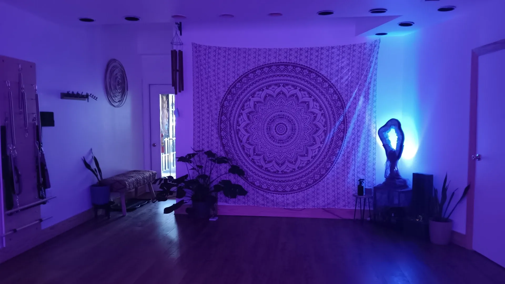 Violet-lit wellness studio with a mandala tapestry, plants, and a glowing crystal lamp