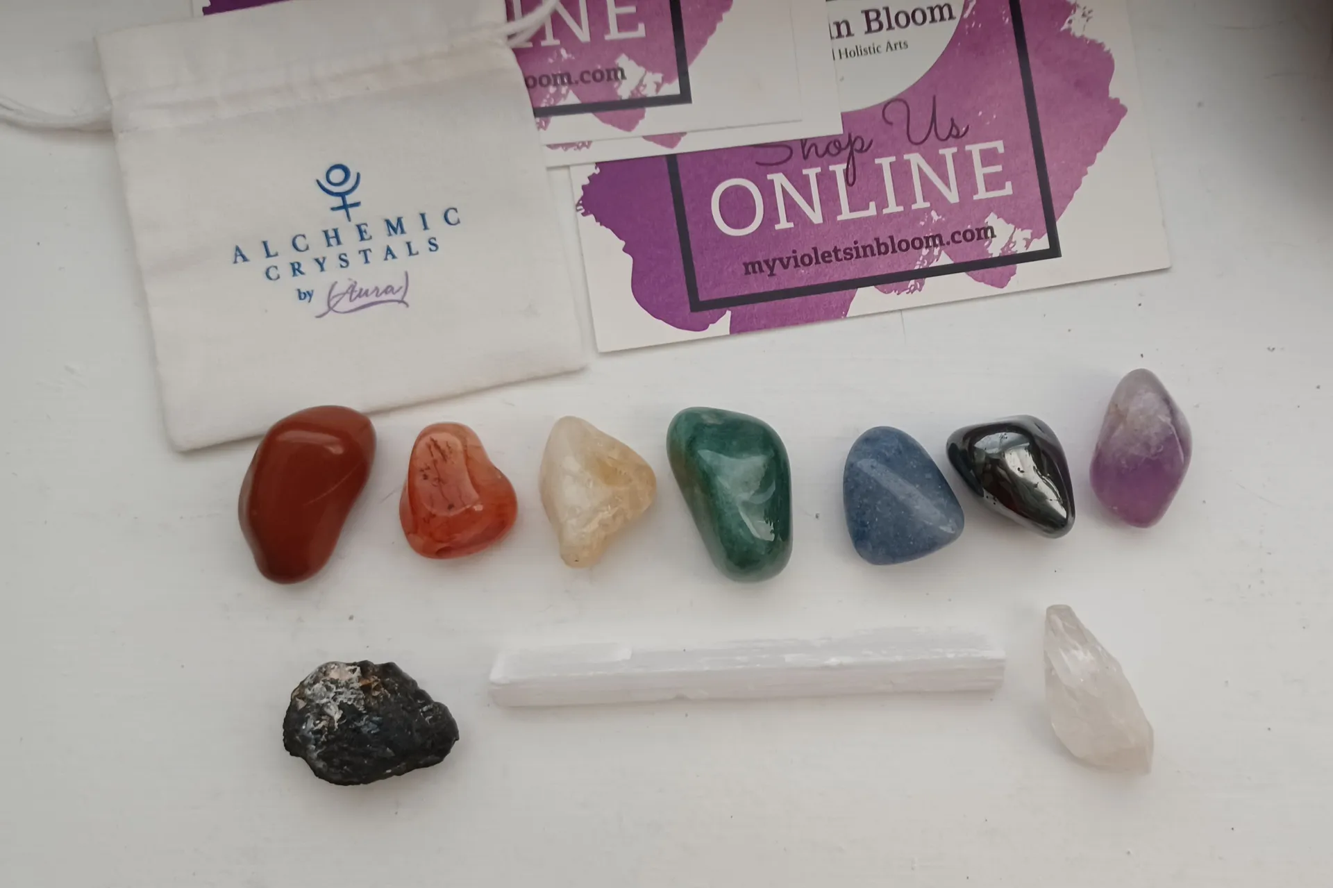 A row of colorful tumbled crystals arranged beside a crystal guide and a small shop card